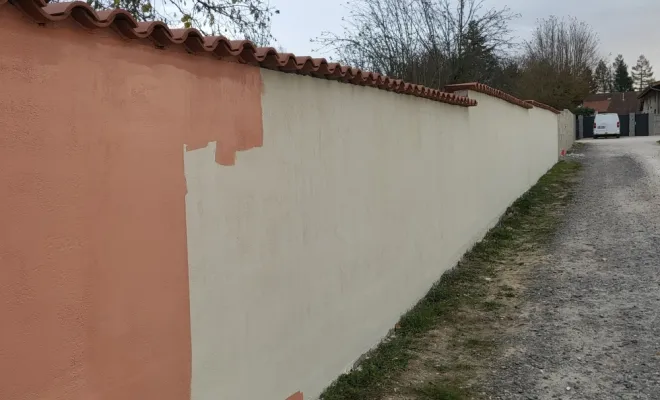 Application de la première couche de peinture façade de fond clair sur mur de clôture à Péronnas